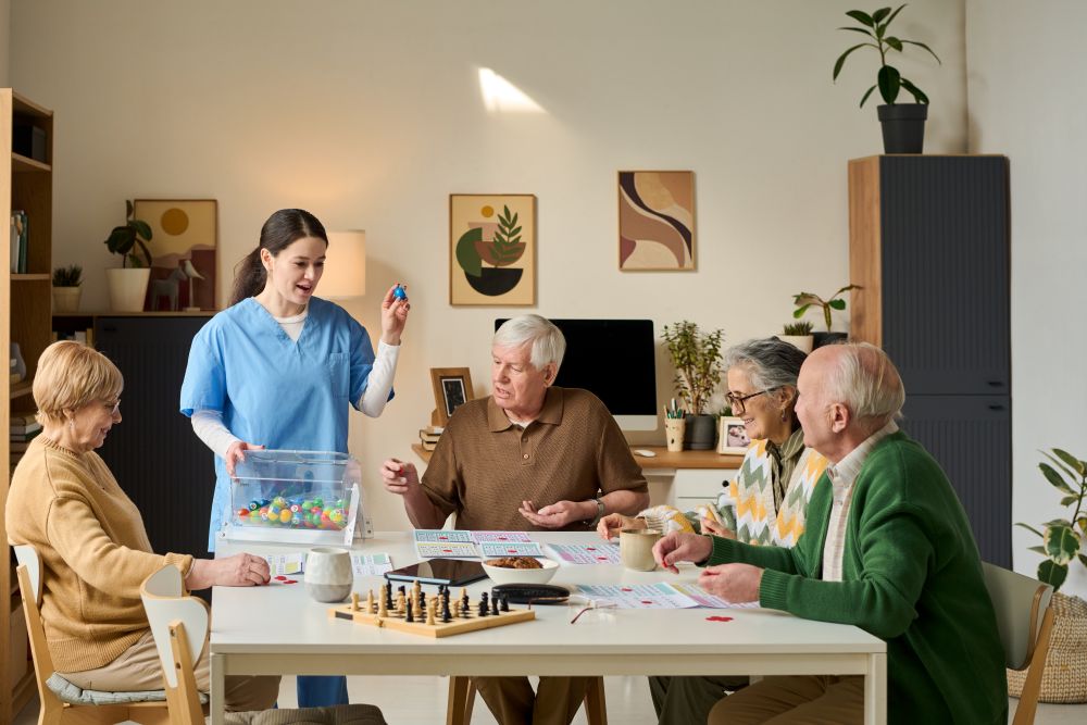 Senior Group Playing Game With Female Caregiver In Care Home