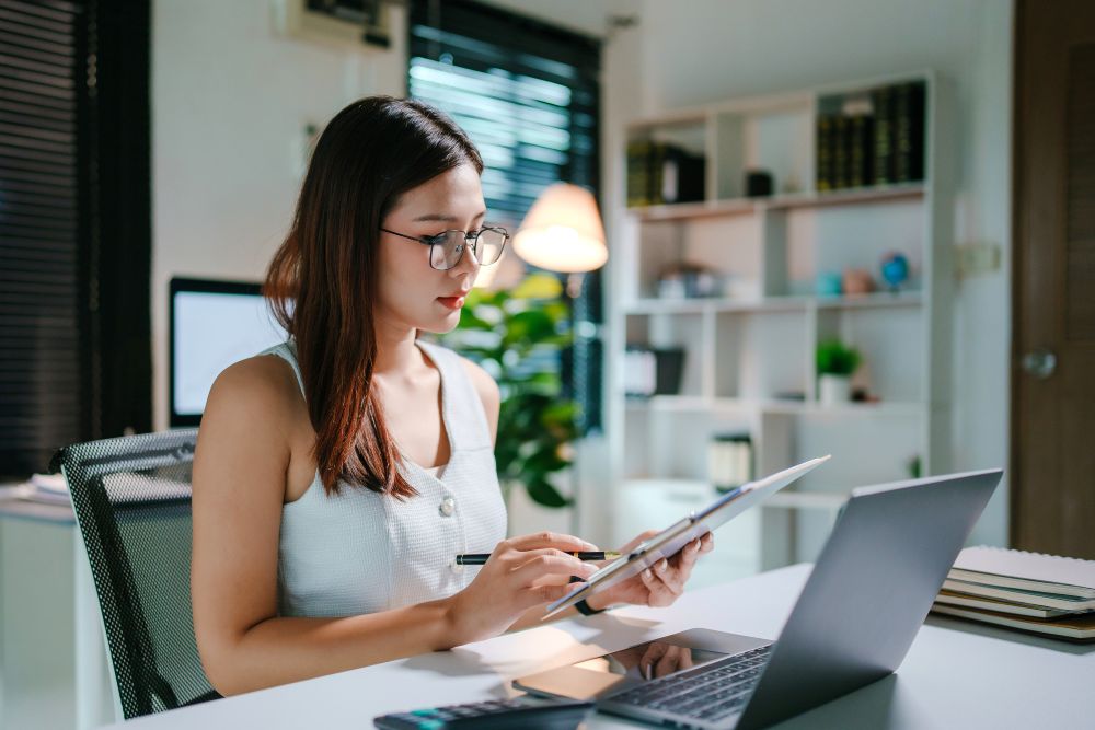 Woman At Desk With Clipboard And Laptop